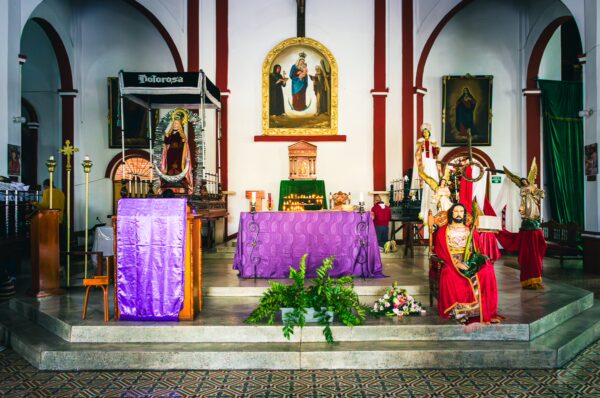 Vibrant altar with purple decorations, religious statues, and candles inside Nuestra Señora del Perpetuo Socorro, Silva, Cauca, Colombia.