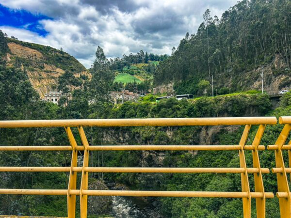 Yellow railing overlooks a lush valley and hillside dotted with greenery near the Rumichaca border between Nariño, Colombia, and Ecuador.