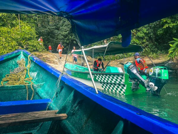 Colorful fishing boats in Uramba, Bahia Malaga, Valle del Cauca, Colombia, with tourists on the shore and lush greenery in the background.