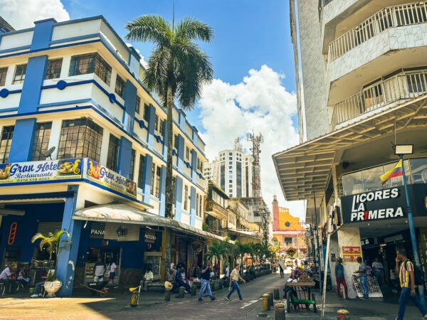 Colorful buildings line the streets of Buenaventura, Valle del Cauca, with people walking and a bright blue sky overhead.