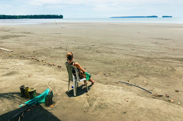 A person sits on a chair at Chucheros Beach in Uramba Bahía Málaga, surrounded by a vast, sandy shoreline and calm waters.