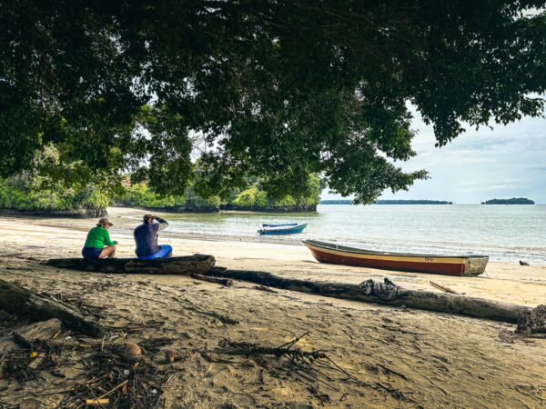 Relaxing at Juan de Dios Beach in Uramba, a tranquil scene with two people sitting under trees by the calm waters of Valle del Cauca.