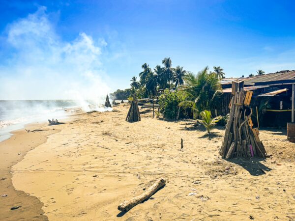 Golden sands and palm trees line the beach in Juanchaco, Valle del Cauca, with smoke rising from a nearby fish camp.
