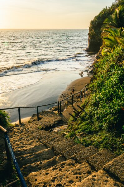 Winding stone steps lead down through lush greenery to the sandy beach and waves of Ladrilleros, Valle del Cauca, Colombia.