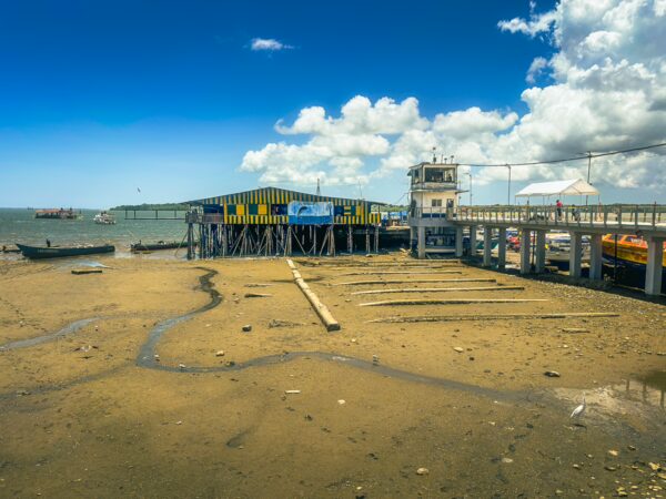 Colorful pier jutting into the sea at Buenaventura, Valle del Cauca, Colombia, surrounded by sandy shore and blue sky.