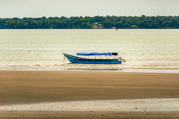 Colorful boat anchored on the sandy shores of Chucheros Beach, with lush greenery along the Uramba Bahia in Valle del Cauca, Colombia.