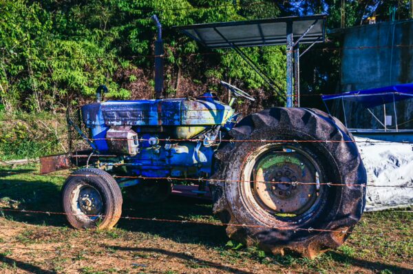 Rusty blue tractor parked on a lush green hillside in Juanchacó, Valle del Cauca, Colombia, surrounded by vibrant vegetation.