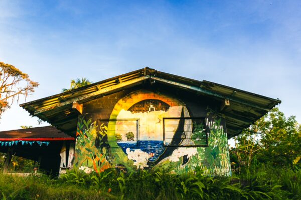 Vibrant mural on a rustic building surrounded by lush greenery in Ladrilleros, Valle del Cauca, Colombia.