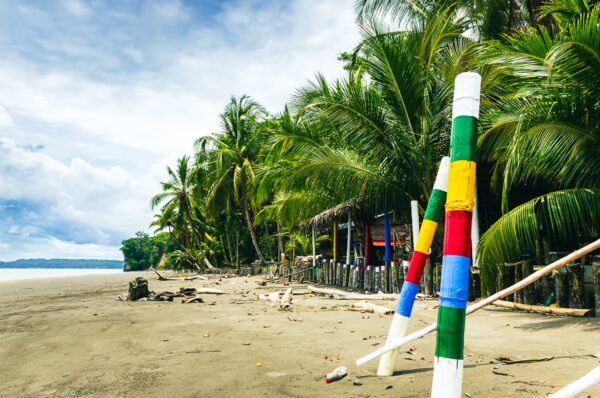 Colorful beach markers stand on the sandy shore of Chucheros Beach, lined with lush palm trees in Uramba, Bahía Málaga, Valle del Cauca.