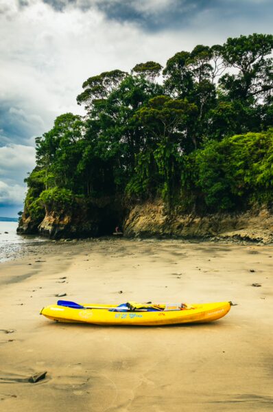 A bright yellow kayak rests on the sandy shore beside lush green cliffs at Juan de Dios Beach in Uramba, Bahía Málaga, Colombia.