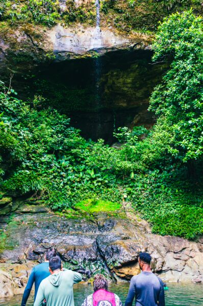 People exploring lush greenery near a cave with a waterfall in La Sierpe, Uramba, Bahía Málaga, Valle del Cauca, Colombia.