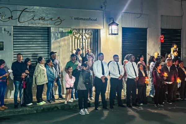Crowd gathered on a street in Popayán, Cauca, Colombia, holding candles and dressed in formal attire during a nighttime event.