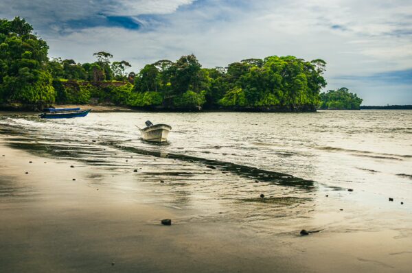 Boats glide across the serene waters of Juan de Dios Beach, surrounded by lush greenery in Uramba, Bahia Malaga.
