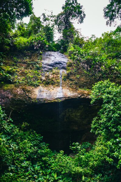 Lush greenery surrounds a small waterfall cascading down a rocky cliff in La Sierpe, Uramba, Valle del Cauca, Colombia.
