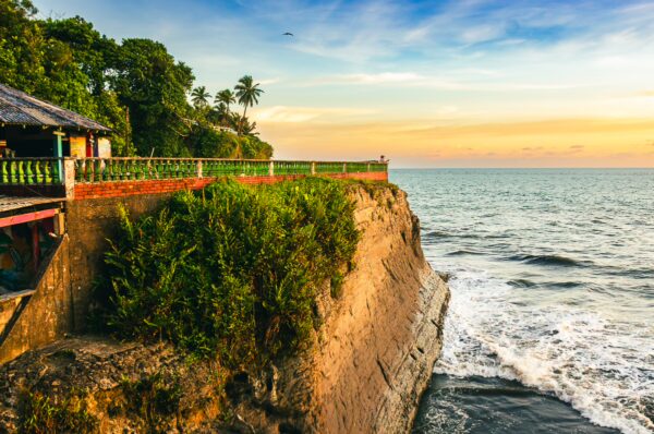 Rugged coastline at Ladrilleros, Valle del Cauca, Colombia, features green vegetation and a vibrant sunset sky over the sea.