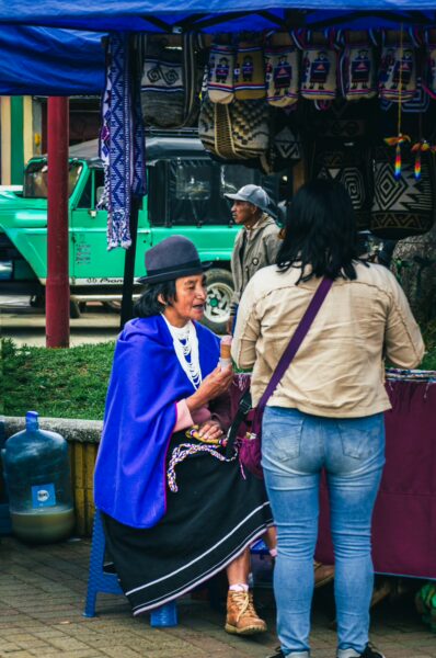 Traditional market scene in Parque Principal Silva, Cauca, Colombia, featuring a woman in a vibrant blue poncho engaging with a visitor.