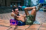 A man gives a thumbs up while lounging on a colorful backpack in Plazoleta de San Francisco, Cali, Valle del Cauca, Colombia.