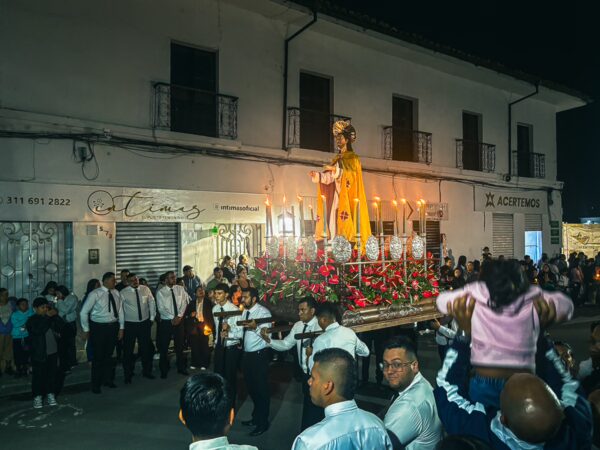 Vibrant evening procession in Popayán, Colombia, featuring a statue adorned with flowers and surrounded by festive participants.