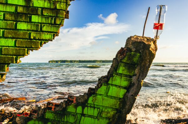 Vibrant green bricks frame a view of the ocean at Juanchaco, Valle del Cauca, with a bottle on the ruins catching sunlight.