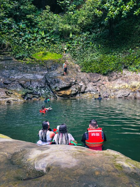 Snorkelers explore the clear waters of La Siepe in Uramba, with lush greenery and rocky formations surrounding the serene pool.