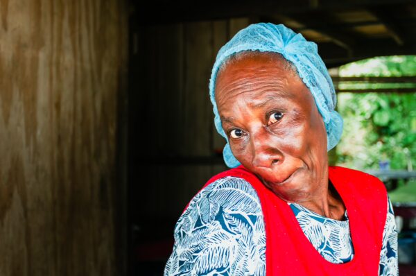 Warm smile of a woman in a red apron and blue headscarf, set against a wooden backdrop in Uramba, Bahía Málaga, Colombia.