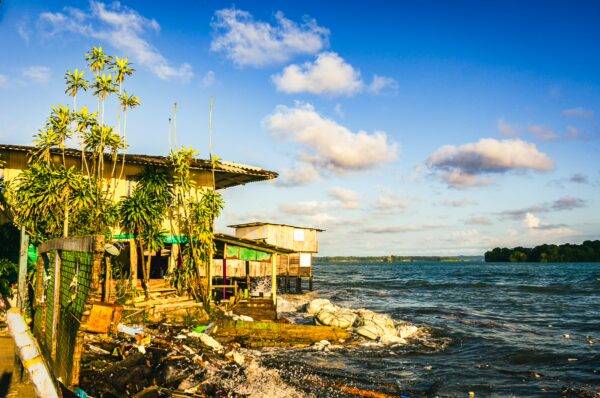 Juanchaco's vibrant coastline features rustic buildings with lush greenery along the water's edge under a blue sky in Valle del Cauca, Colombia.