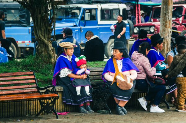 Colorful traditional clothing worn by women with children in Parque Principal Silva, Cauca, Colombia, surrounded by local vendors and visitors.