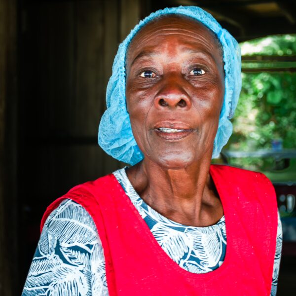 A woman wearing a blue headscarf and red apron stands in a rustic setting near Chucheros Beach, Uramba, Bahía Málaga, Valle del Cauca.