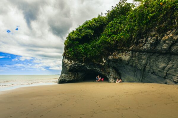 Juan de Dios Beach features dramatic cliffs and lush greenery, with visitors relaxing on the sandy shore in Uramba, Bahía Málaga.
