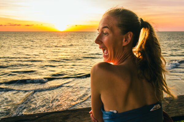 A woman with a ponytail smiles joyfully at the vibrant sunset over the waves at Ladrilleros, Valle del Cauca, Colombia.