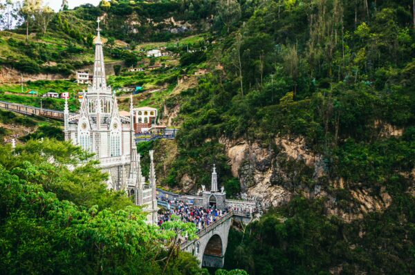 Basilica de Las Lajas, nestled in lush hills, features intricate architecture and a bustling bridge in Narino, Colombia.