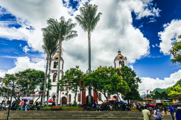 Vibrant scene at Parque Principal Silva in Cauca, Colombia, featuring lush palms, a lively crowd, and dramatic clouds.