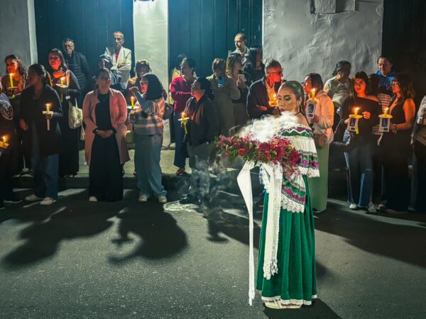 Colorful procession in Popayán, Cauca, Colombia, with participants holding candles and a woman adorned in traditional attire at the forefront.