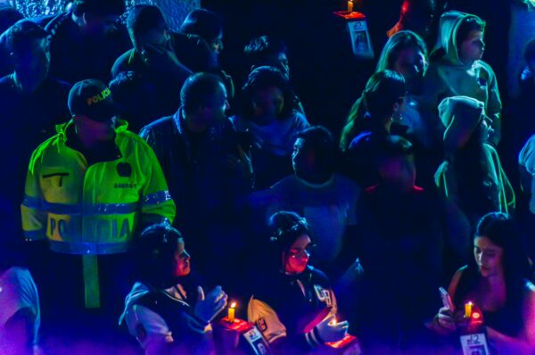 Crowd gathered in vibrant colors holding candles during an event in Popayán, Cauca, Colombia, with a visible police presence.
