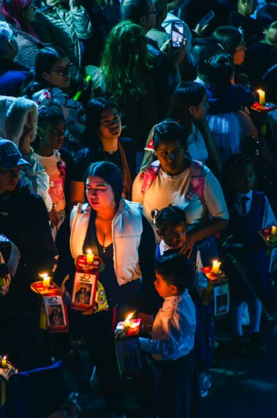 Candlelight procession in Popayán, Cauca, Colombia, featuring participants holding candles and portraits, amidst a vibrant crowd.