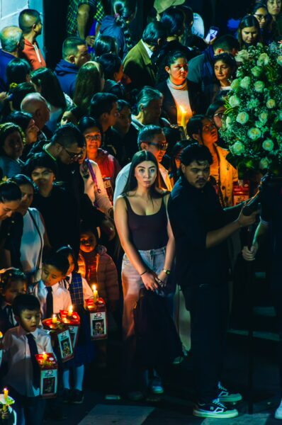 Crowd gathered in a vibrant procession holding candles, with a young woman in a white dress at the center in Popayán, Cauca, Colombia.