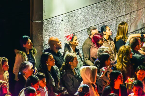 Crowd of diverse individuals gathered, eagerly watching an event, illuminated by colorful lights in Popayán, Cauca, Colombia.