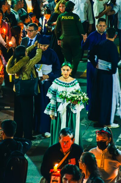 Festive procession in Popayán, Colombia, featuring a woman in traditional attire holding flowers amidst a vibrant crowd.