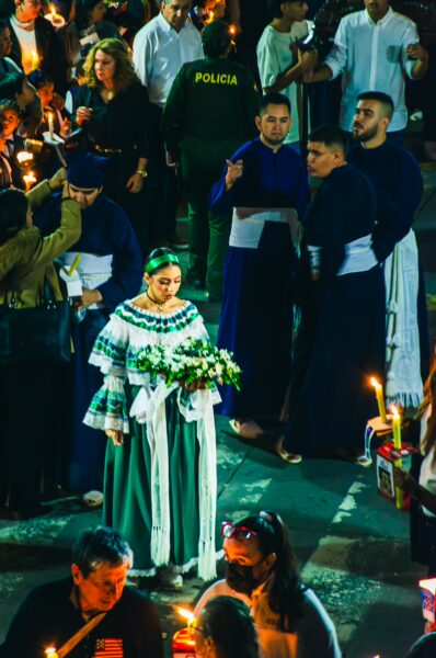 Traditionally dressed woman holding flowers surrounded by a festive crowd, celebrating in Popayán, Cauca, Colombia.