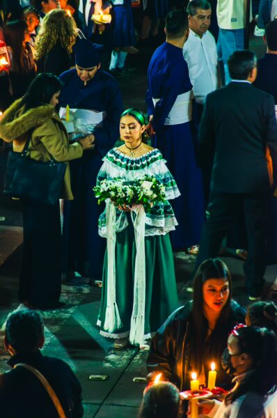 Festively dressed woman in traditional attire holds flowers amidst a vibrant gathering in Popayán, Cauca, Colombia.