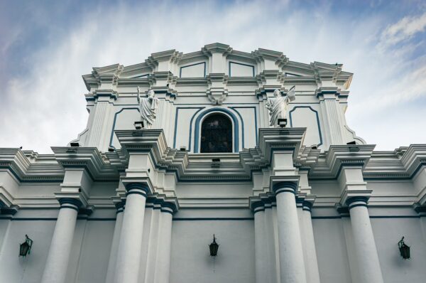 Assumption Cathedral features elegant white architecture with ornate detailing and tall columns against a cloudy sky in Popayán, Cauca.