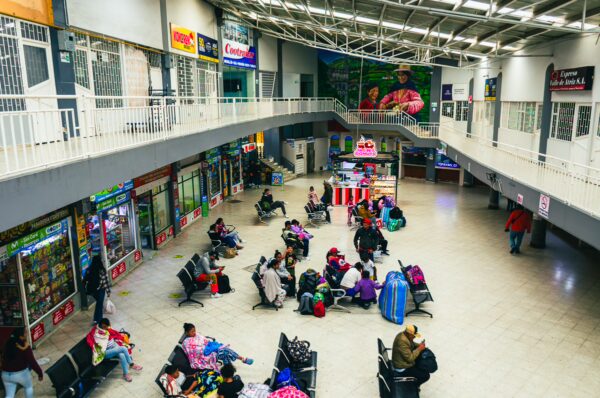Busy bus terminal in Ipiales, Narino, Colombia, featuring travelers seated in waiting areas among shops and bright advertisements.