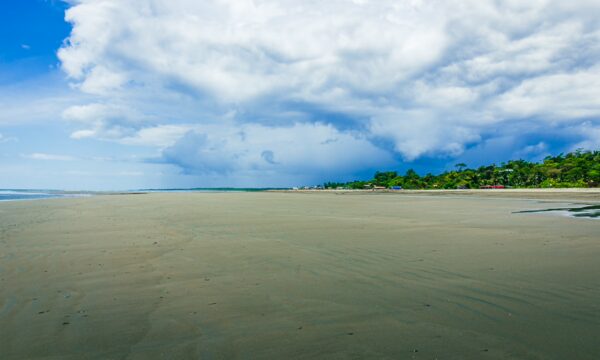 Golden sands stretch across the shore at La Barra, Valle del Cauca, Colombia, under a dramatic sky filled with clouds.