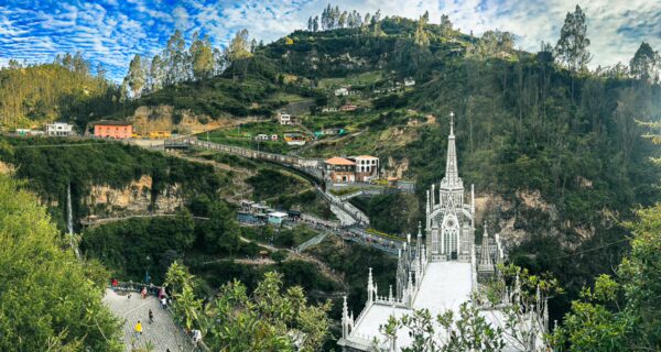 Stunning view of Las Lajas Sanctuary nestled in a lush green valley, surrounded by mountains and a winding road in Narino, Colombia.