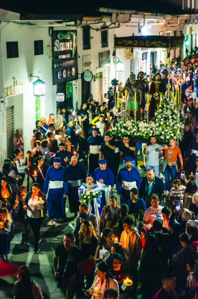 Vibrant procession with participants in blue robes and candles, celebrating a night festival in Popayán, Cauca, Colombia.