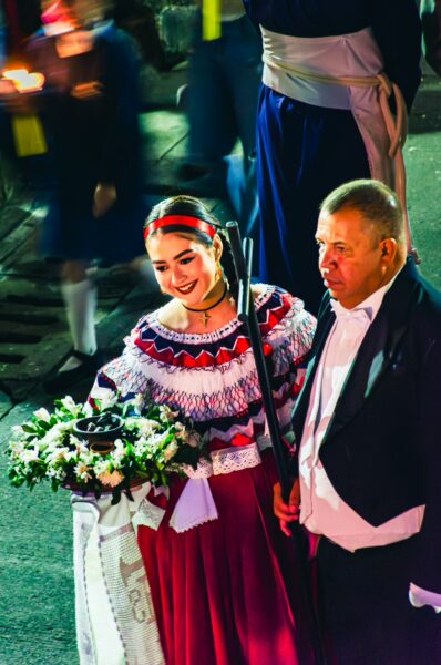Traditional dancers in colorful costumes, celebrating a festival in Popayán, Cauca, Colombia, with floral arrangements in hand.
