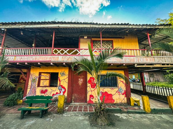 Colorful building with vibrant murals and a green bench in Juanchaco, Valle del Cauca, Colombia, under a bright blue sky.