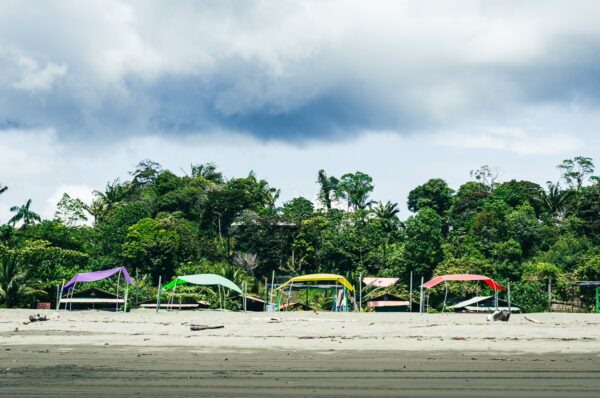 Colorful beach canopies lined along the sandy shore, surrounded by lush greenery in La Barra, Valle del Cauca, Colombia.