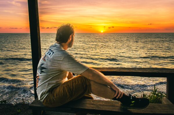 Admiring a sunset over the ocean, a traveler sits on a wooden bench in Ladrilleros, Valle del Cauca, Colombia.