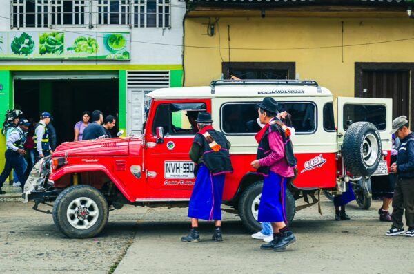 Vibrant red jeep parked in Cauca, Colombia, with local villagers in traditional attire gathering nearby.
